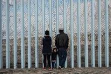 Nicole Cruz y David García observan hacia el lado estadounidense del muro junto a su hijo de dos años, Mateo García. La familia García decidió huir de Honduras debido a amenazas de la pandilla Barrio 18.
