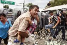 Un padre corre despavorido con su hijo en brazos mientras los policías federales disuaden a la multitud de centroamericanos que intentaba ingresar al territorio mexicano tras forzar la apertura del segundo portón.