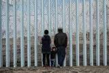 Nicole Cruz y David García observan hacia el lado estadounidense del muro junto a su hijo de dos años, Mateo García. La familia García decidió huir de Honduras debido a amenazas de la pandilla Barrio 18.