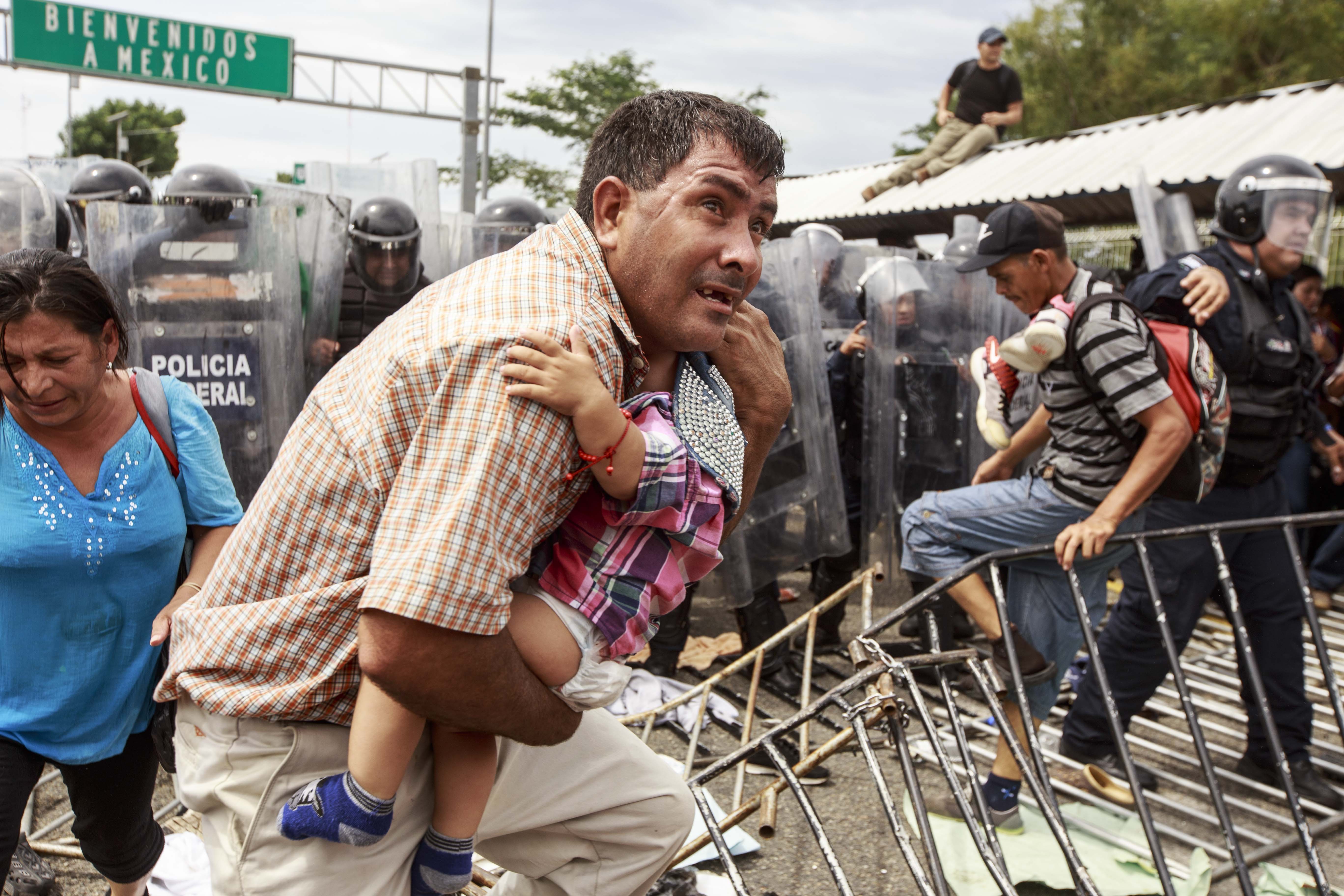 Los éxodos de refugiados en América. Un padre corre despavorido con su hijo en brazos mientras los policías federales disuaden a la multitud de centroamericanos que intentaba ingresar al territorio mexicano tras forzar la apertura del segundo portón.