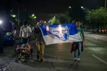 Con una bandera de la Selección Nacional de Fútbol de Honduras, dos jóvenes encabezan un grupo que no superaba las 200 personas y que salió en la madrugada desde la Terminal Metropolitana de Buses de San Pedro Sula. 31 de enero de 2020. Foto: Martín Cálix.