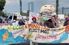 Mujeres marchando con una manta en la que se leé "Ecofeministas, juntas resistimos y florecemos"