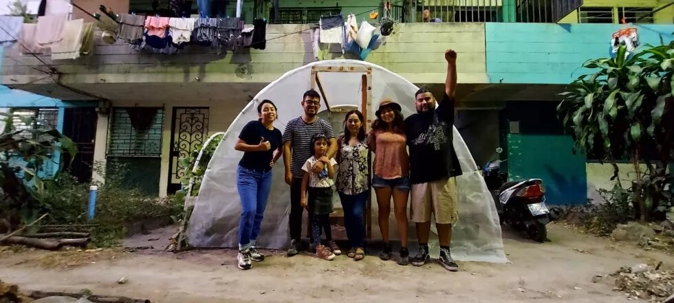 Jovenes en zona suburbana frente a un pequeño invernadero. 