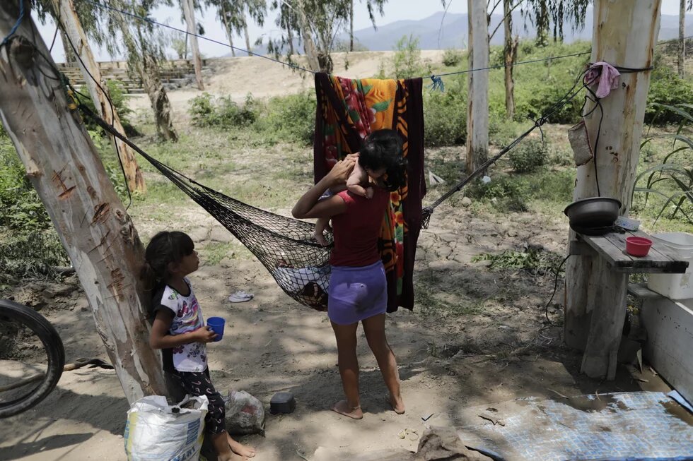 Mujer campesina de espaldas carga a un niño en un espacio improvisado como casa