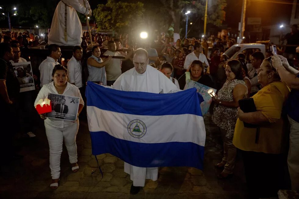 El padre Edwin Román, párroco de la Iglesia San Miguel en Masaya, cargo una bandera de Nicaragua durante la procesión del silencio que se realiza el  jueves santo. En la procesión también participaron familiares de los muertos y de los presos políticos. Debido a la labor humanitaria que Román realiza, ha recibido amenazas de muerte, es por eso que  desde junio del año pasado posee medidas cautelares por parte de la CIDH. 18 de abril de 2019. Foto: Fred Ramos